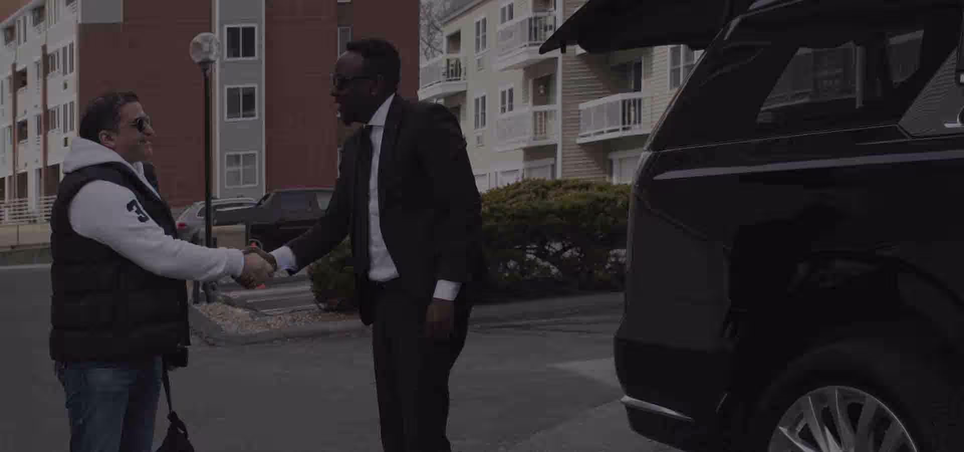 Professional limousine Chauffeur greeting a corporate client next to a luxury suv escalade in Boston, MA downtown financial district